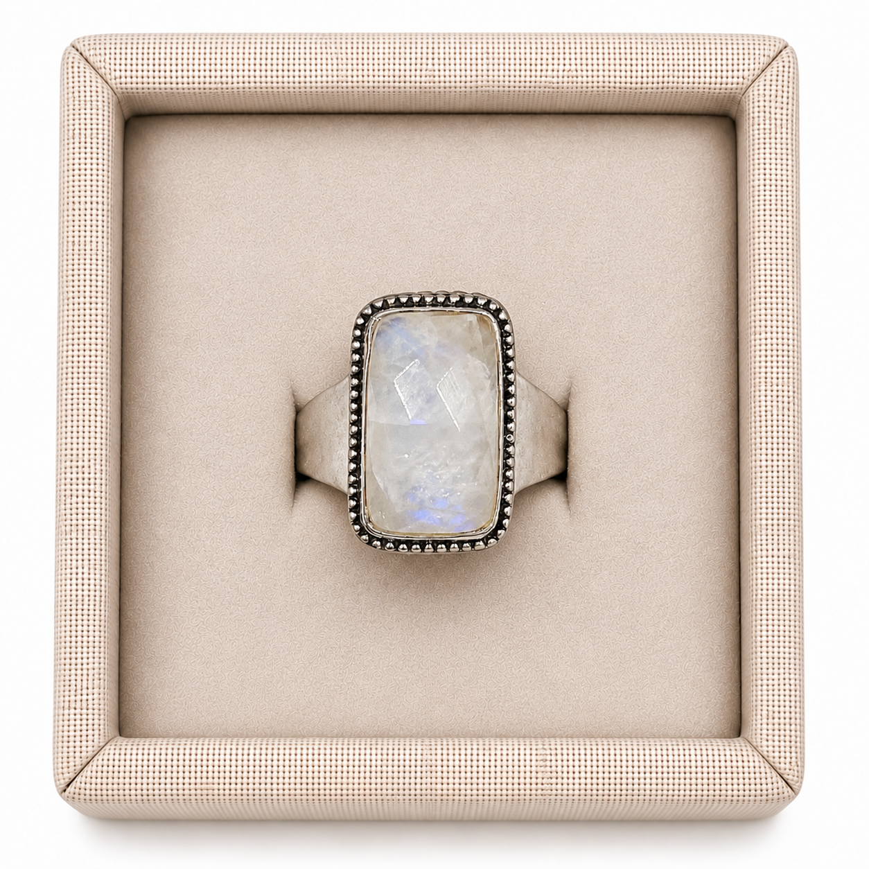 A faceted rectangular Rainbow Moonstone is set in a clean sterling silver bezel, allowing the stone's natural adularescence to take center stage. The geometric cut catches light with subtle, shifting movement. In a decorative linen box on a white background -Clover's Charm.