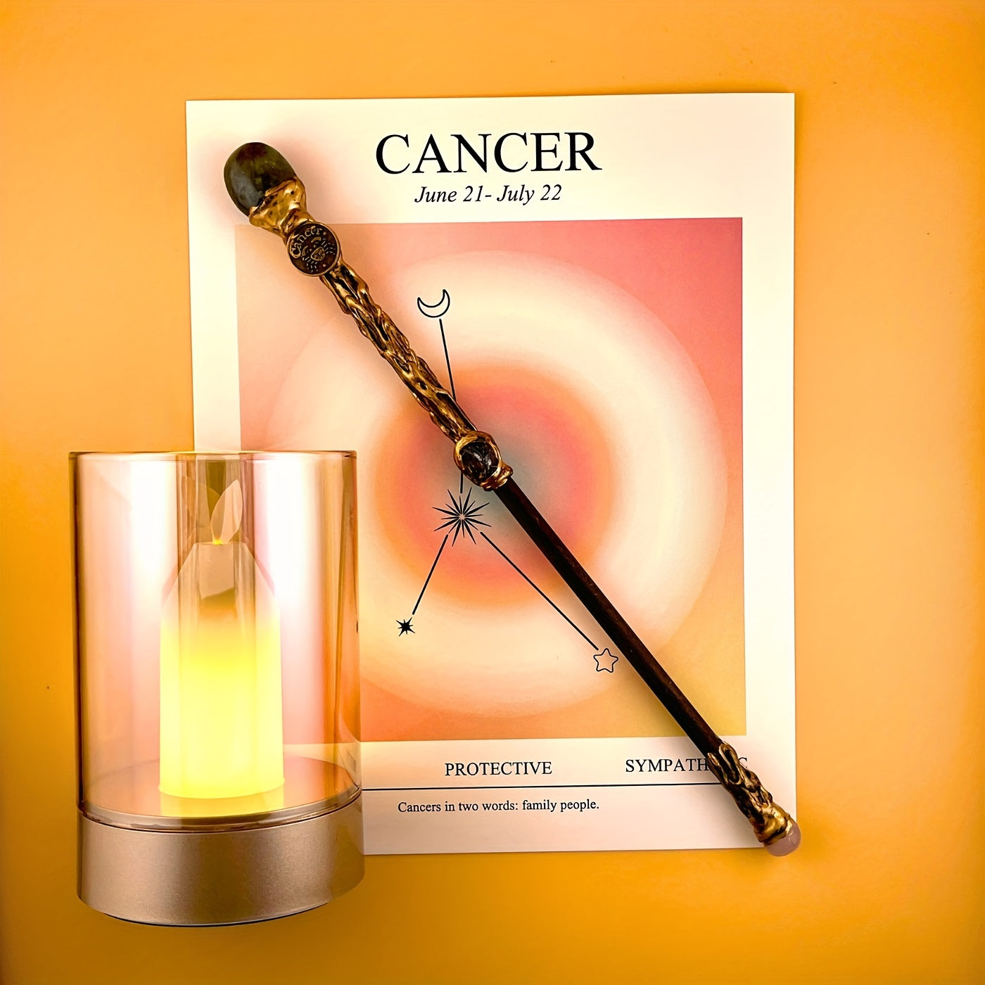 Cancer zodiac art print with constellation design displayed beside a glass candle holder and decorative astrology wand on a warm yellow background