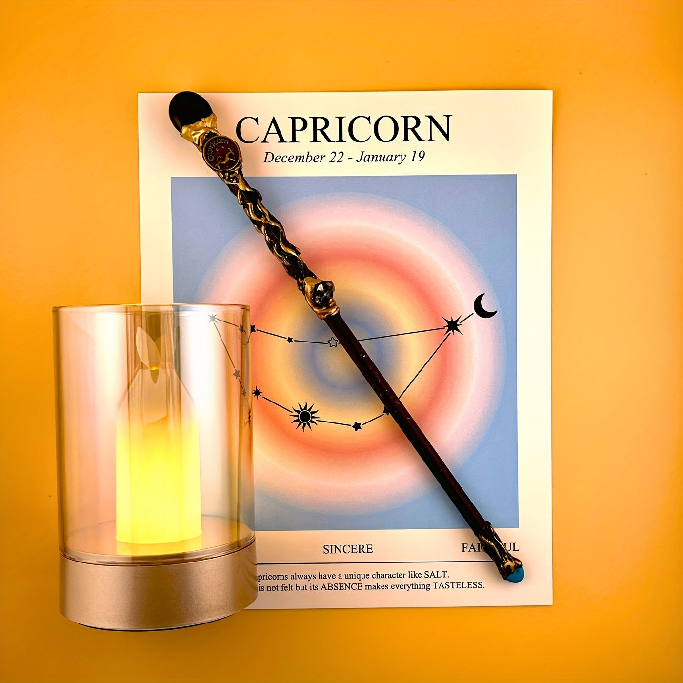 Capricorn zodiac art print with constellation design displayed beside a glass candle holder and decorative astrology wand on a warm yellow background