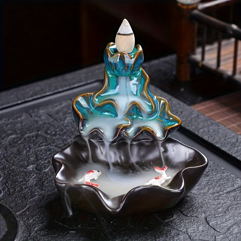 Front view lotus blue ceramic incense burner with a cone incense burning and incense smoke flowing down like a waterfall. Twin fish detailing at the basin base

