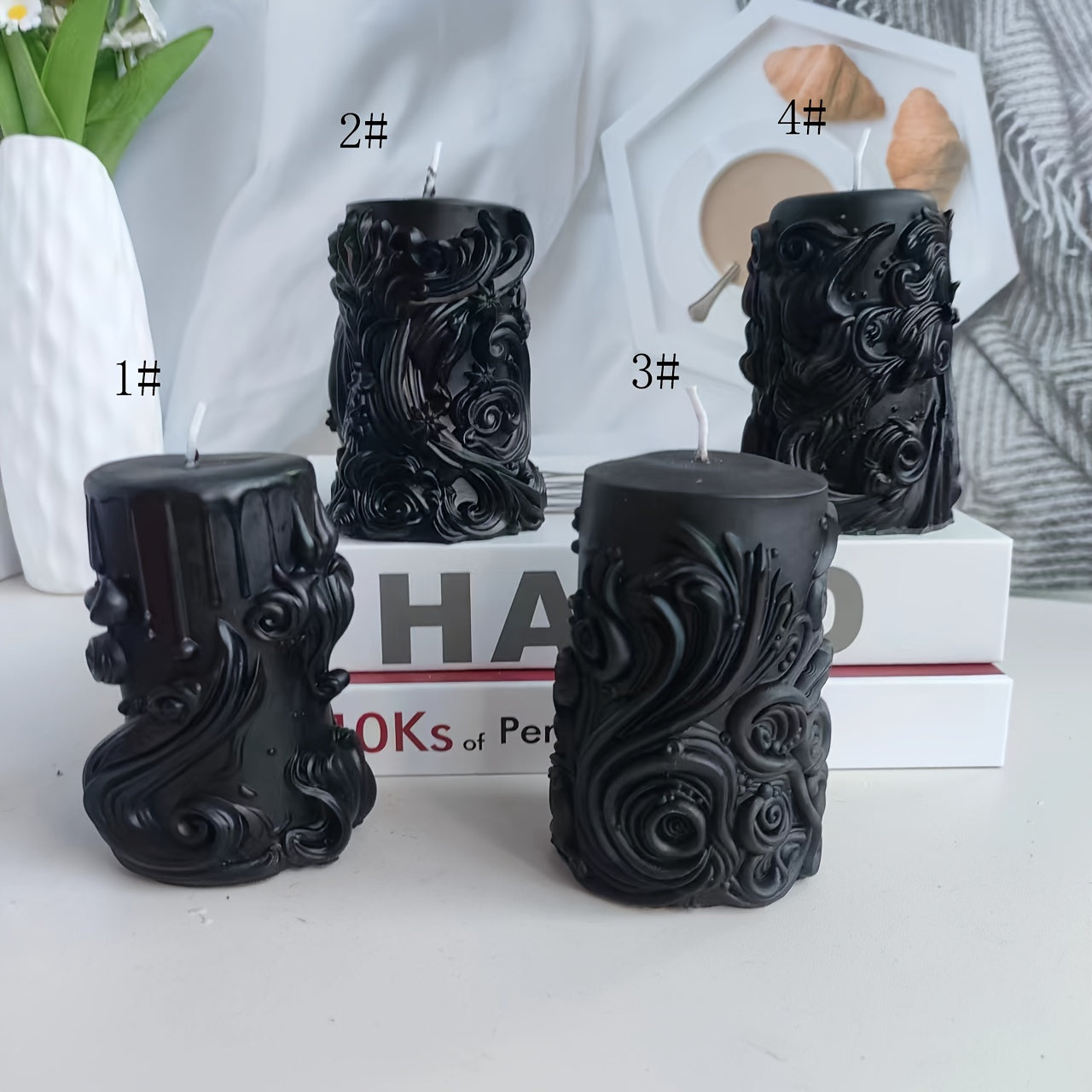 Black sculpted pillar candles with ornate floral and swirl detailing displayed in four design variations on a styled tabletop with books and decor accents