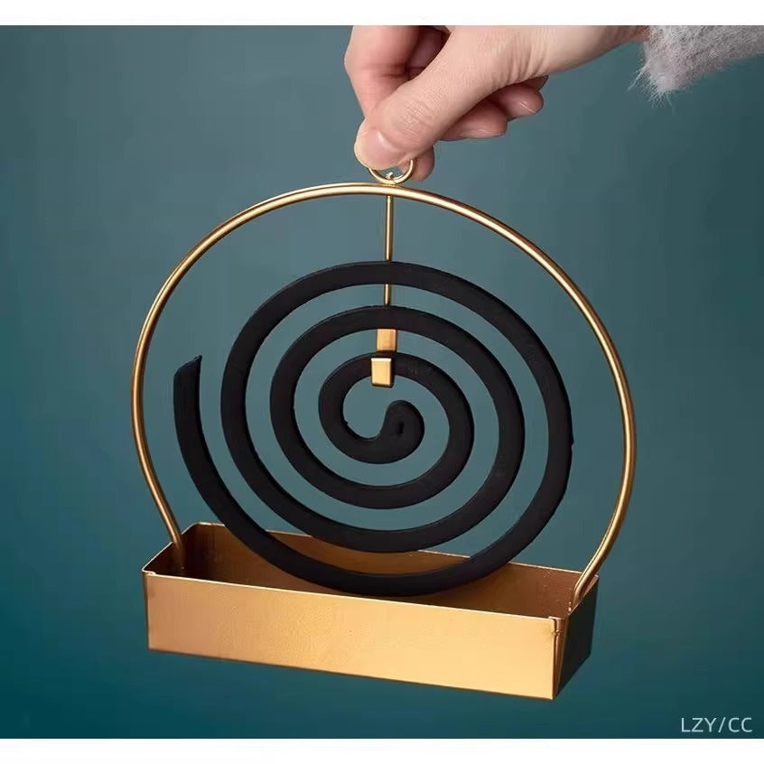 Hand placing spiral incense coil into gold metal incense burner tray with hanging frame and a rectangle tray attached at the bottom.