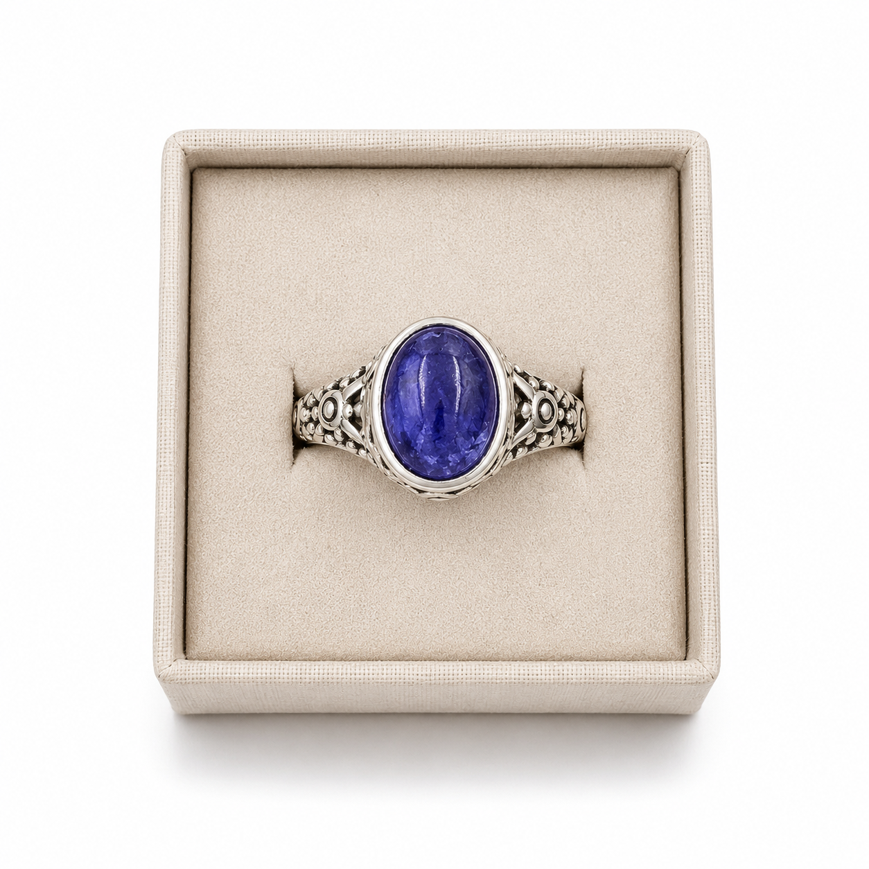 Sterling silver oval tanzanite ring with ornate filigree band displayed in a soft linen jewelry box on a white background -Clover's Charm.