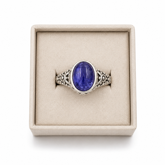 Sterling silver oval tanzanite ring with ornate filigree band displayed in a soft linen jewelry box on a white background -Clover's Charm.