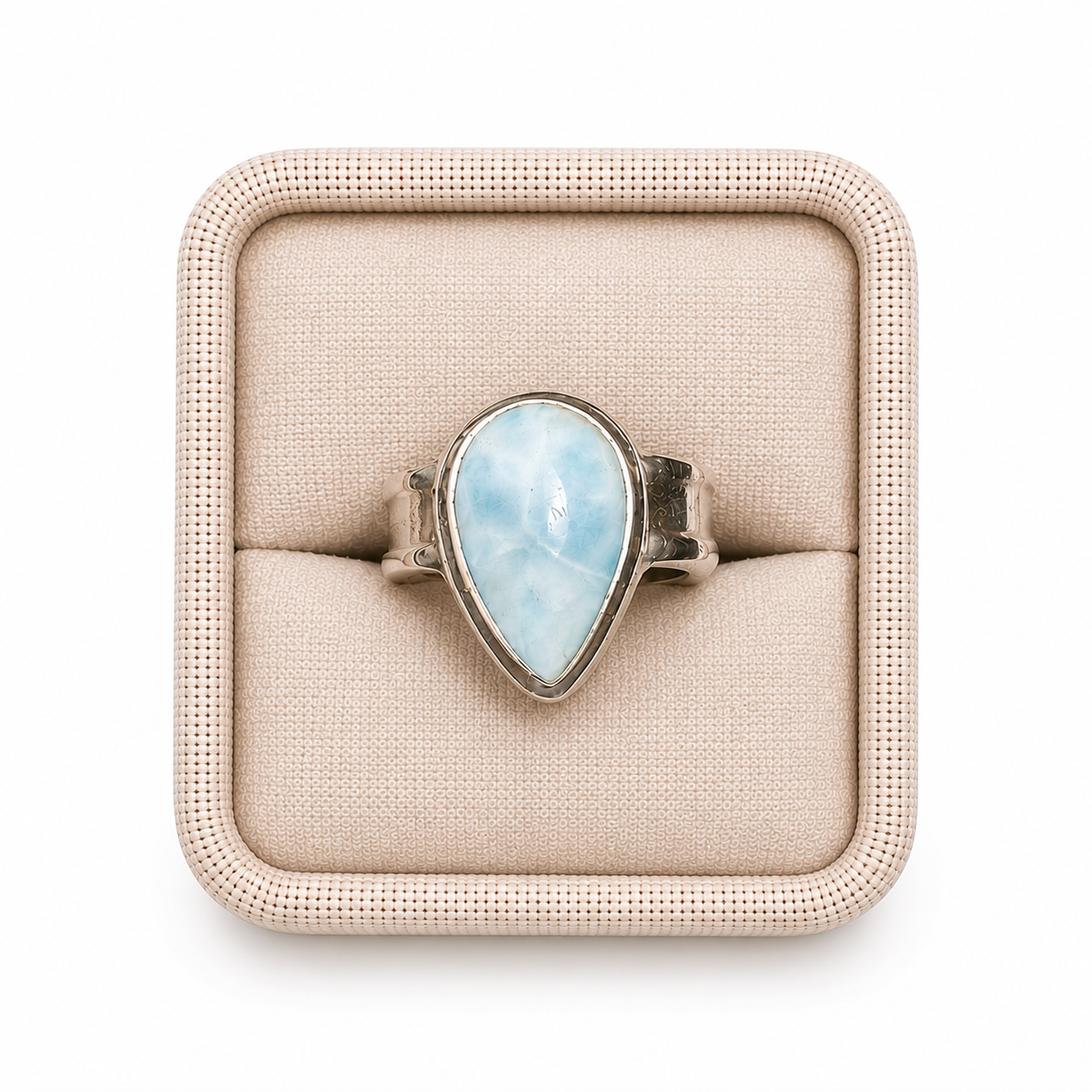 A graceful teardrop Larimar cabochon is securely bezel-set in polished sterling silver, its flowing silhouette echoing the gentle movement of water. Clean, sculptural lines give the ring a contemporary elegance, while the smooth bezel allows the stone's tranquil blue and white marbling to remain the unmistakable focal point. Sitting in a linen box on a white background -Clover's Charm.