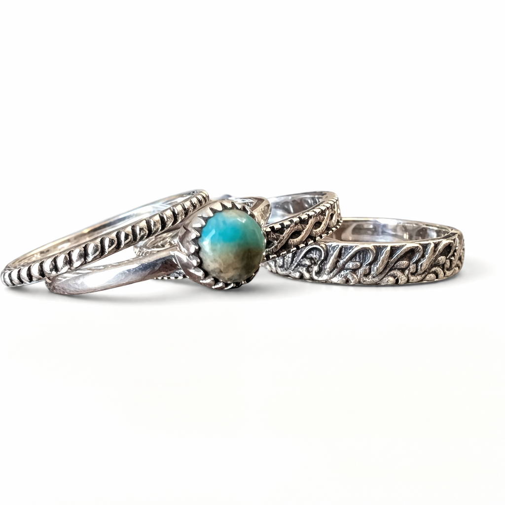 Four sterling silver stacker rings with intricate designs spread out on a white background