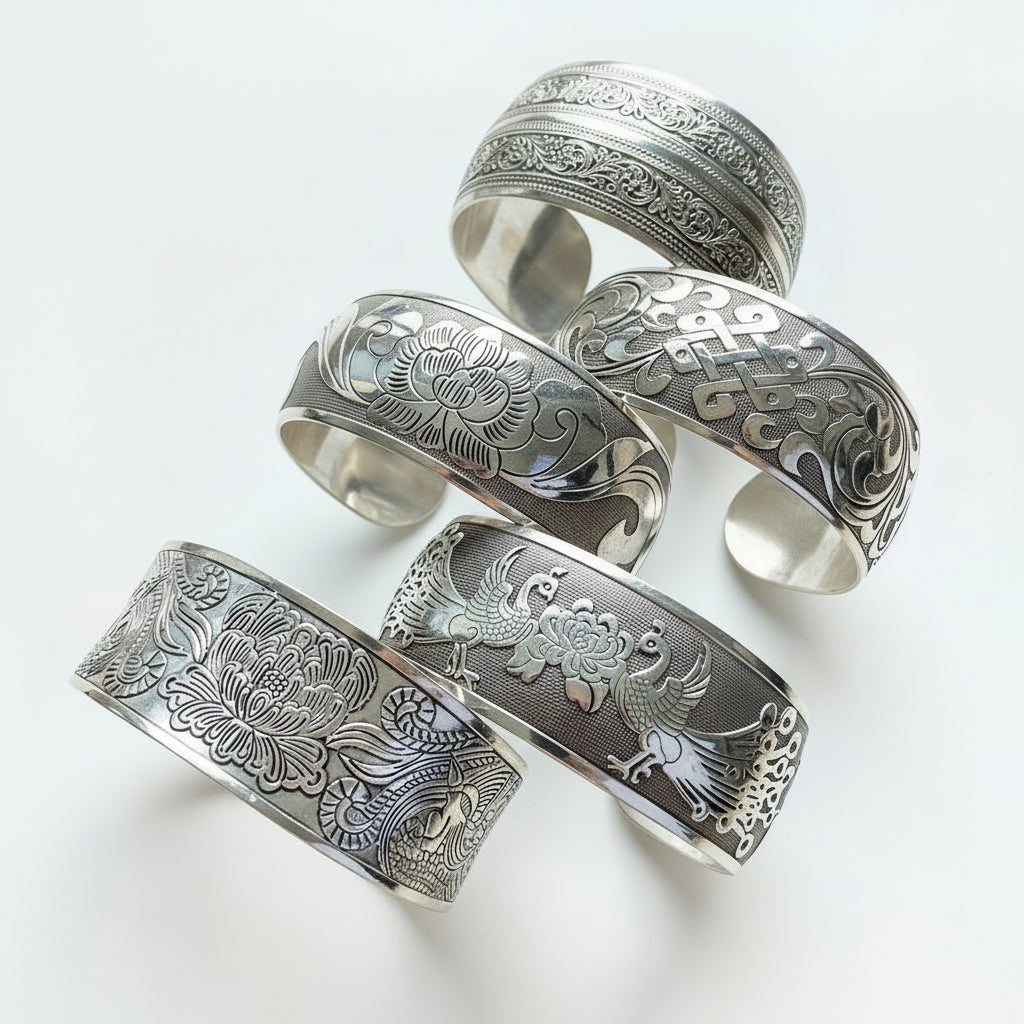 Silver cuffs with intricate designs on a dark surface
