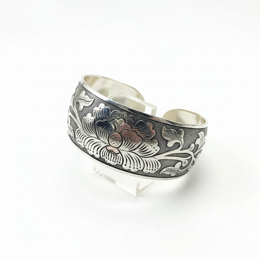 Silver cuff bracelet with intricate designs on a wooden stand against a dark background