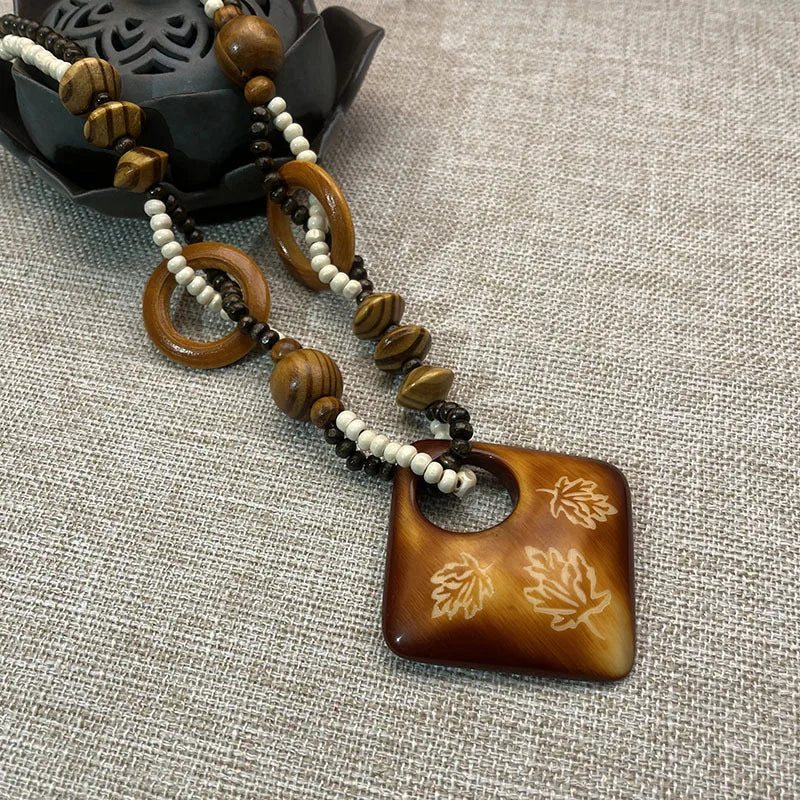 Necklace with brown pendant and beads on a textured surface with leaf patterns in a diamond shape