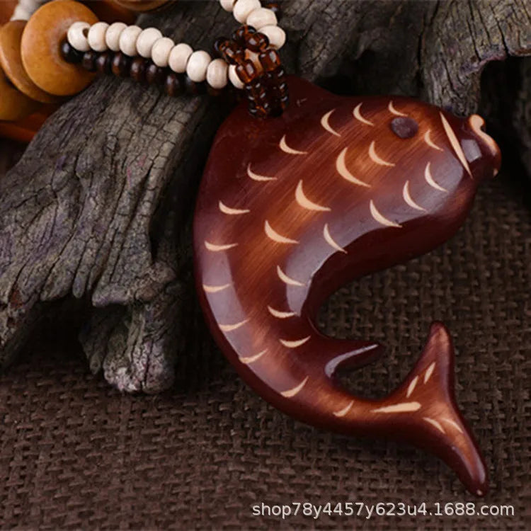 Wooden fish-shaped pendant on a textured surface with beads