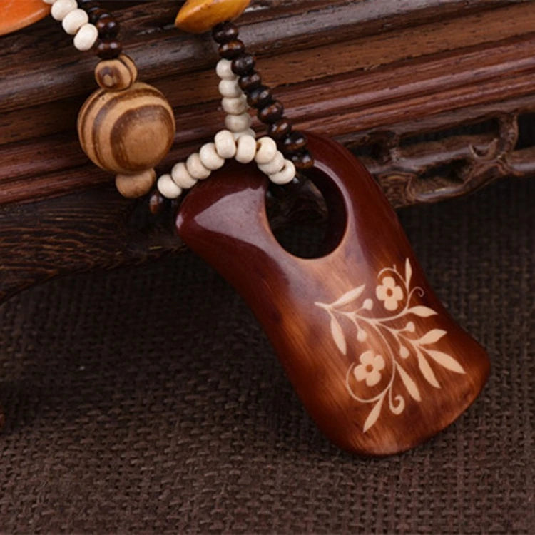 Wooden pendant with floral engraving on a beaded necklace against a wooden background