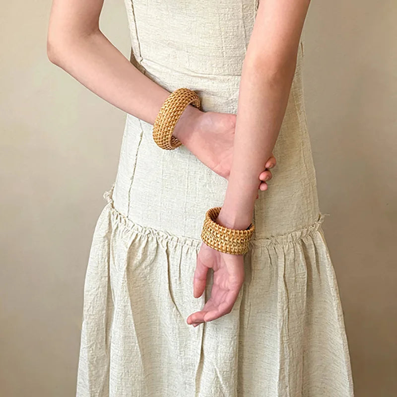 Person standing wearing a beige dress with woven bangles on a neutral background