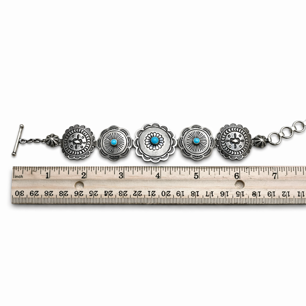 A sterling silver Concho link bracelet with Sleeping Beauty turquoise stones and a toggle clasp, aka T-bar clasp, spread out next to a ruler measuring 1-8 inches on a white background.