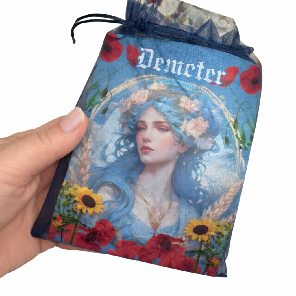 Hand holding a drawstring bag with 'Demeter' design featuring a woman and flowers.