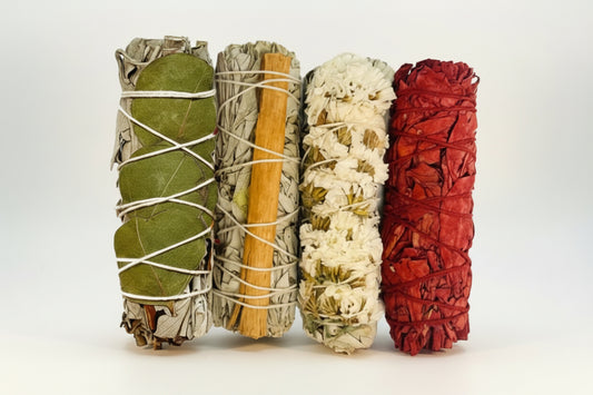 Four bundles of sage, each with different colored bands and materials, on a white background.