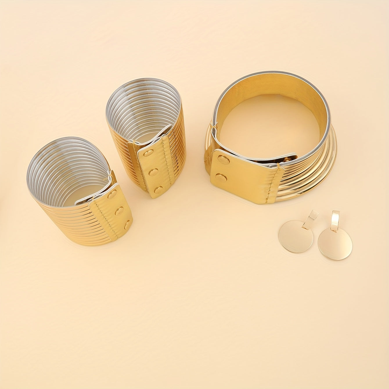 Gold look cuff bracelets and earrings on a beige background