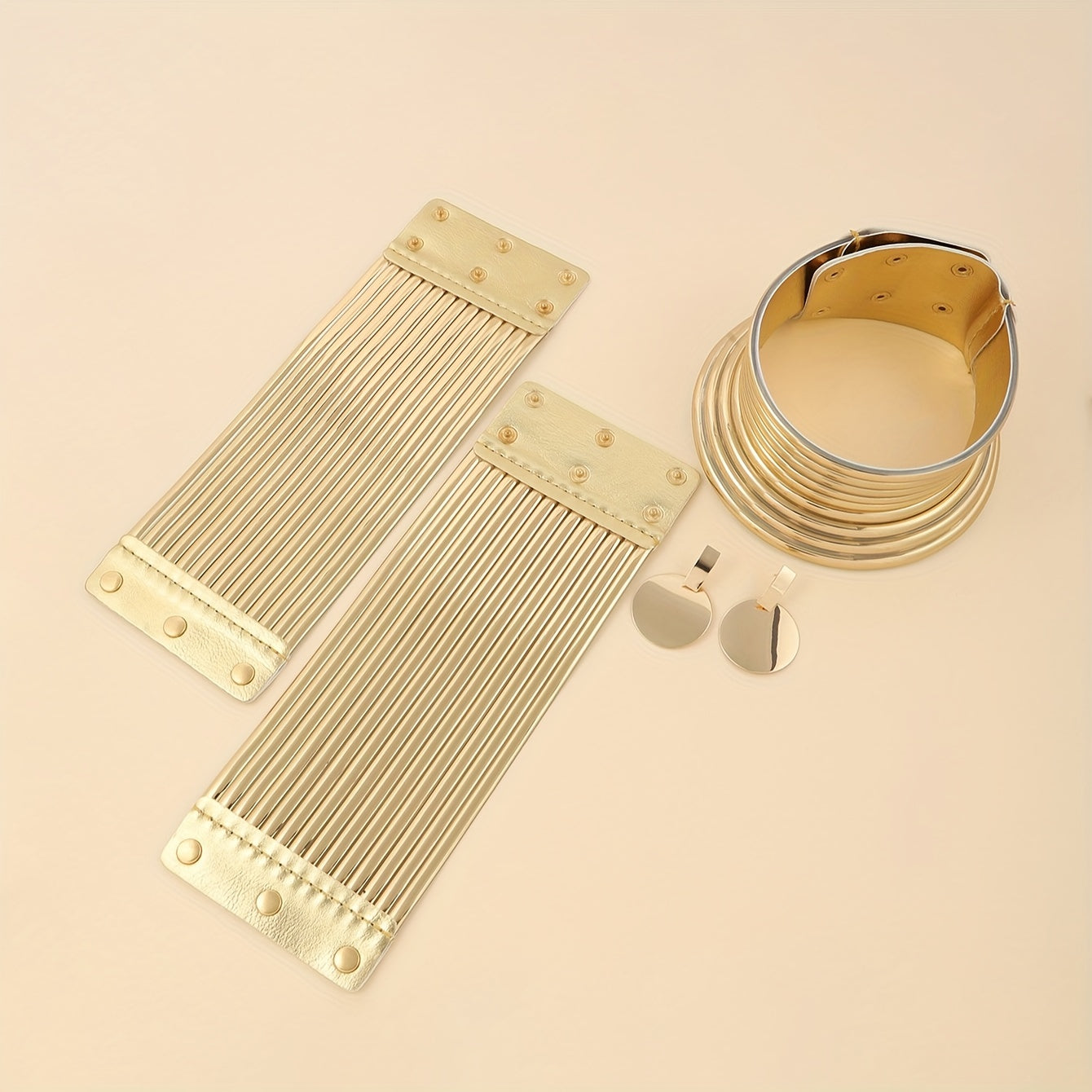 Gold look jewelry set including a bracelet, necklace, and earring on a beige background