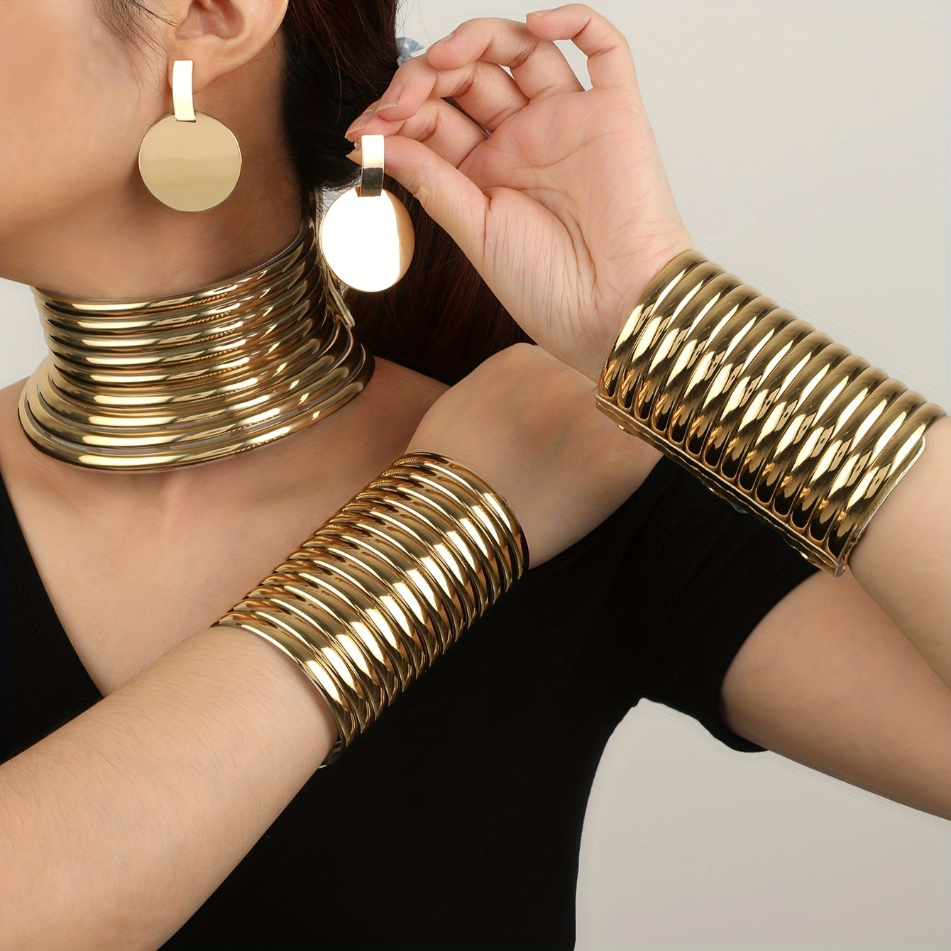 Gold look jewelry set including choker, earrings, and bracelets on a neutral background