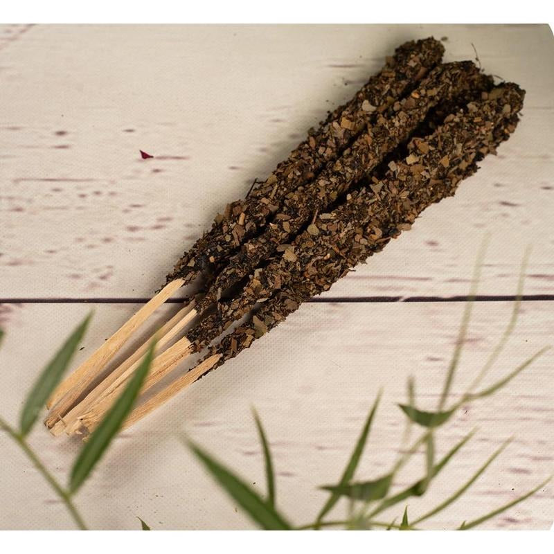Pile of incense sticks with a dark, textured material on a light wooden surface.