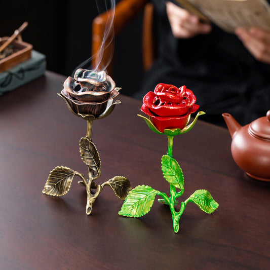 Decorative rose-shaped incense burners on a wooden surface with a person reading a book in the background.