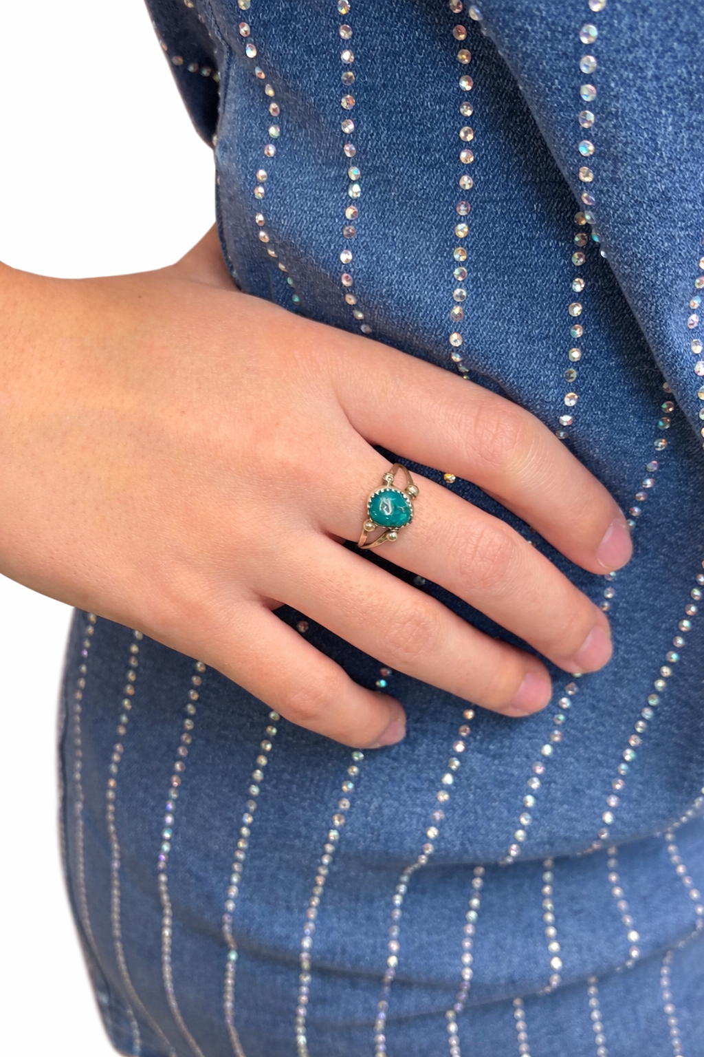 Hand wearing a ring with a blue-green gemstone against a blue pinstripe fabric background