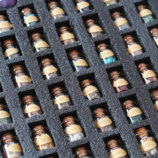 Collection of small bottles filled with gemstones with labels arranged in a grid on a black foam block.