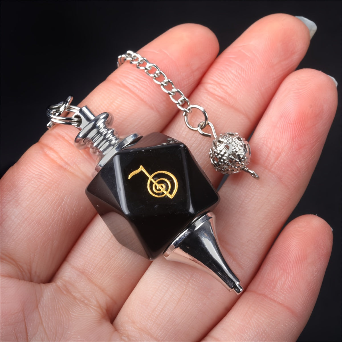 Black and silver pendulum with a chain held in a hand against a dark background