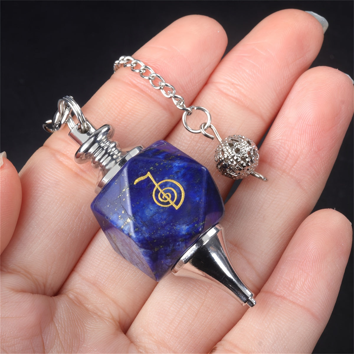 Blue crystal pendant with a yellow symbol held in a hand against a dark background