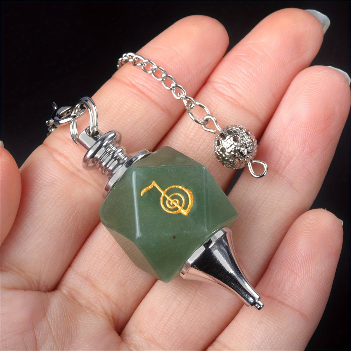 Green polyhedral die pendant with chain held in a hand against a dark background