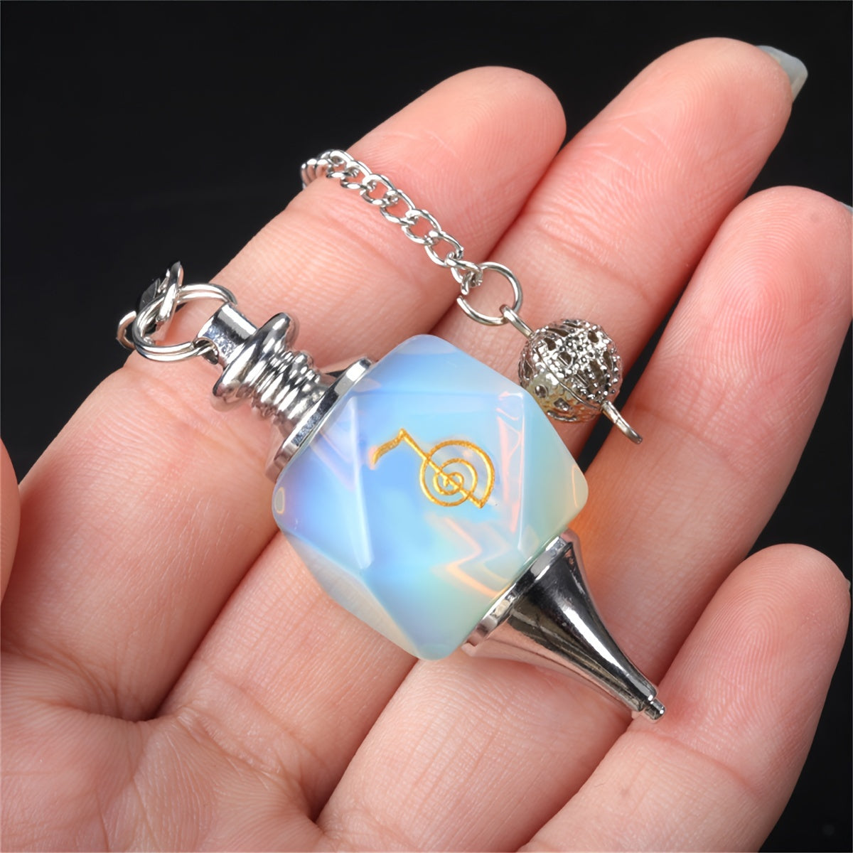 Opalite pendulum with silver chain held in a hand against a black background