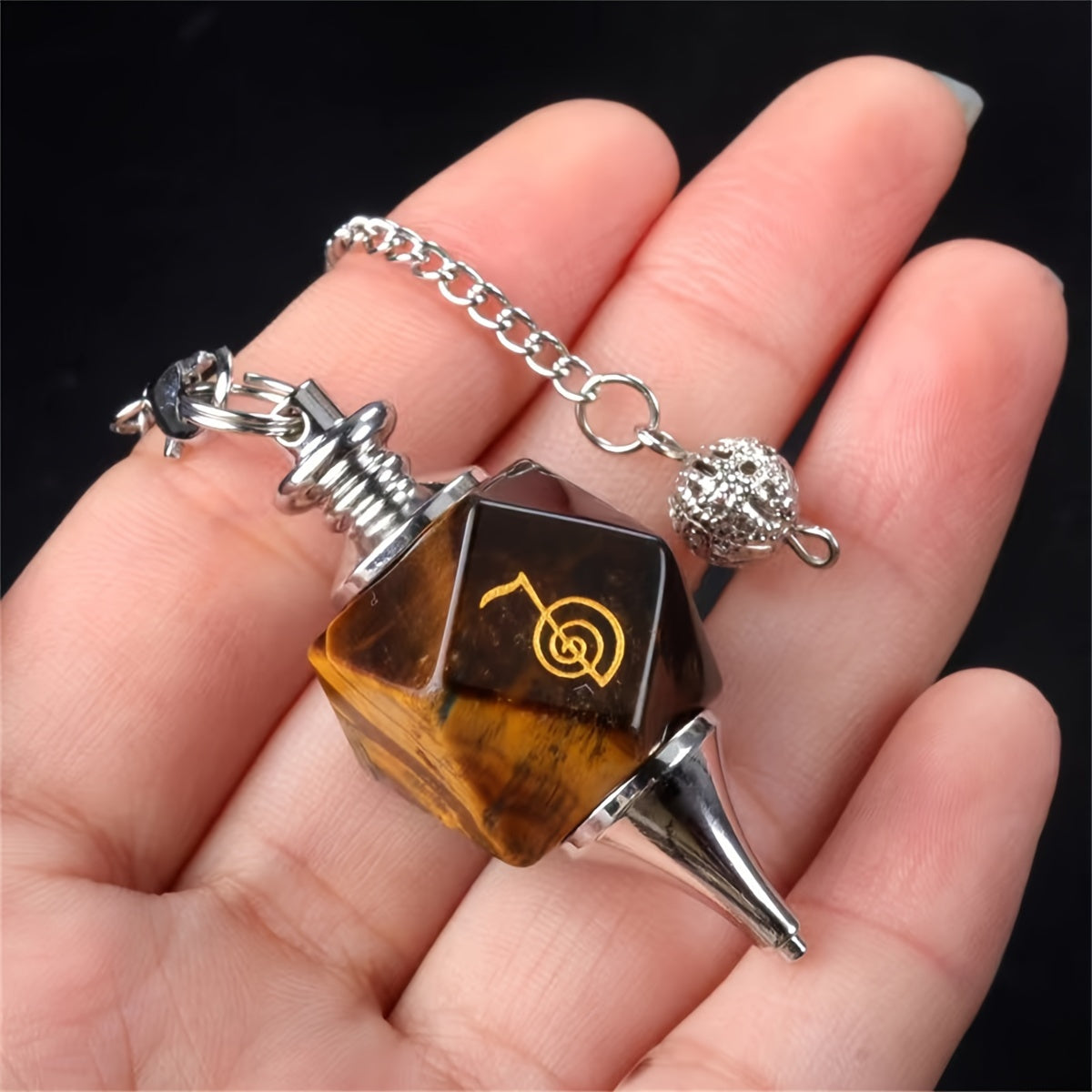 Hand holding a unique tigers eye pendant with a chain against a dark background