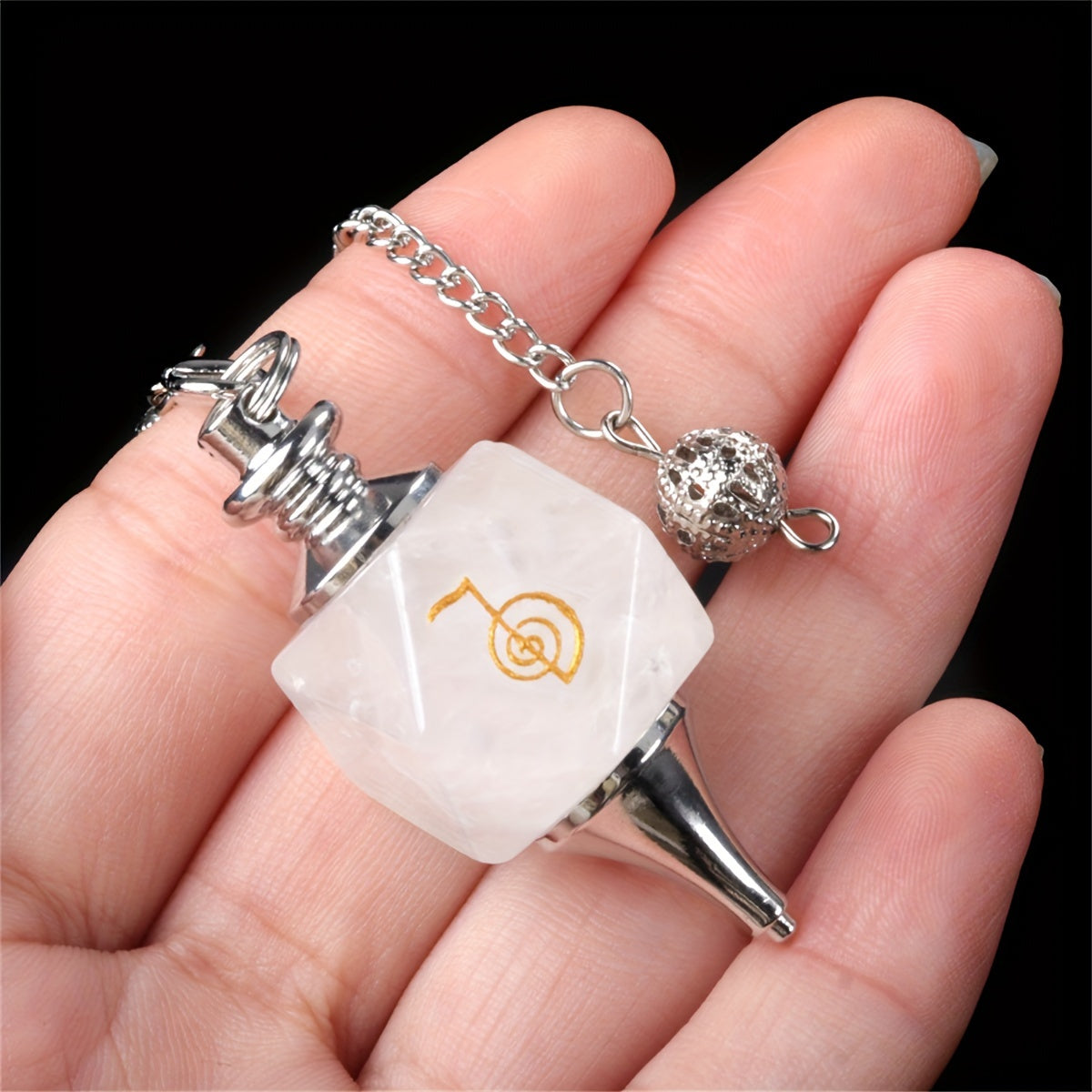 White stone pendant with silver chain held in a hand against a black background