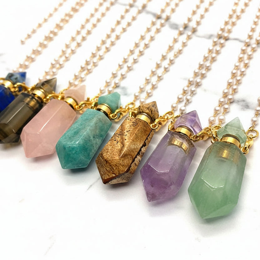 7 Assorted natural gemstone prism perfume bottle necklaces with gold plated chains on a white marble surface