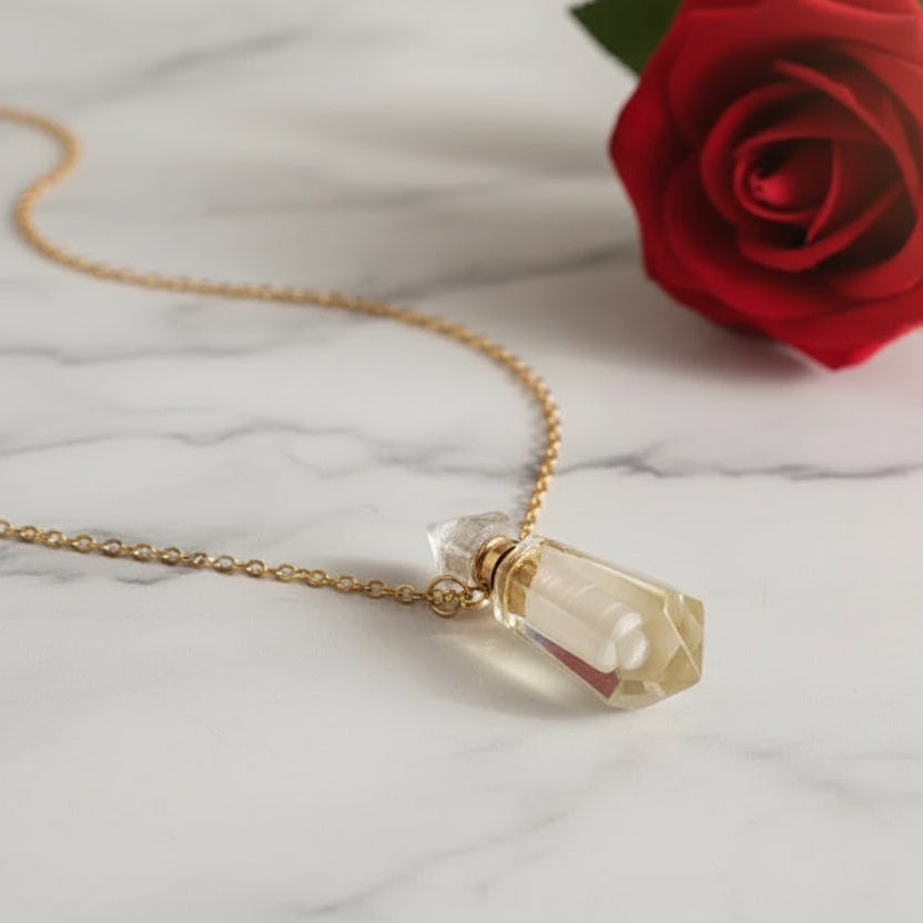 Natural Gems Stone Faceted Prism Perfume Bottle Pendant and chain on a white marble surface next to a red rose.