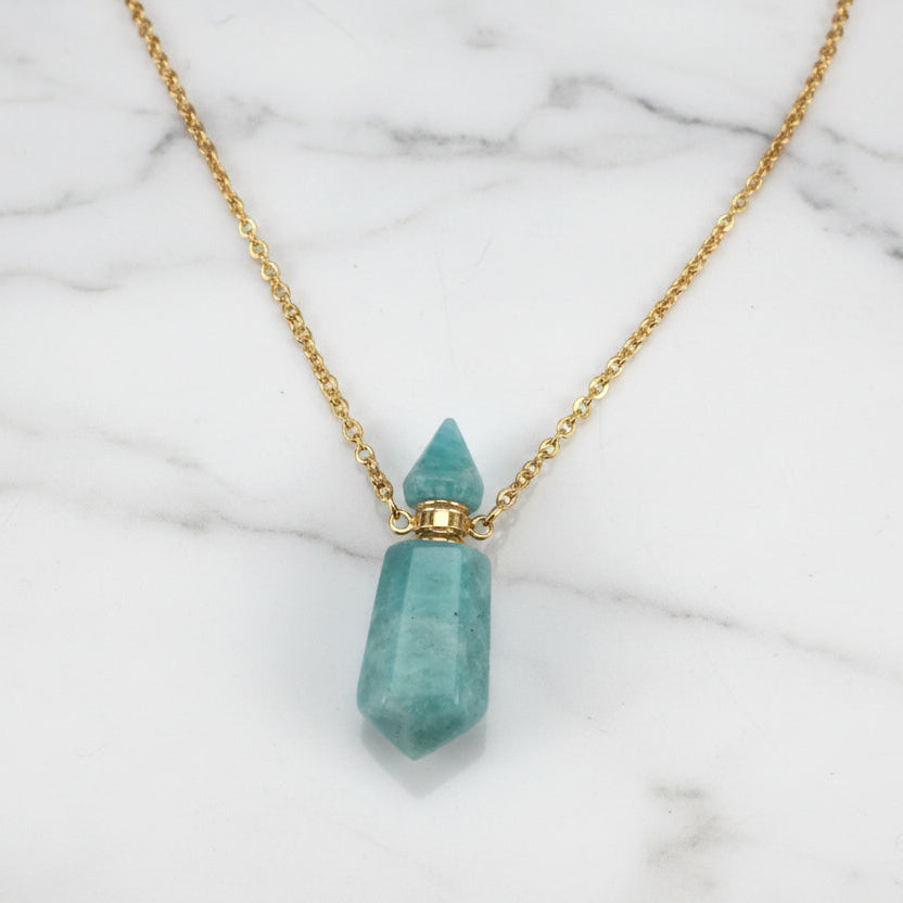 Natural gemstone prism perfume bottle necklaces with gold plated chains on a white marble surface