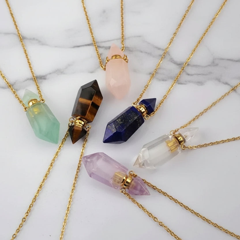 Assorted natural gemstone prism perfume bottle necklaces with gold plated chains on a white marble surface.