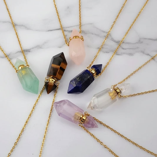 Assorted natural gemstone prism perfume bottle necklaces with gold plated chains on a white marble surface.