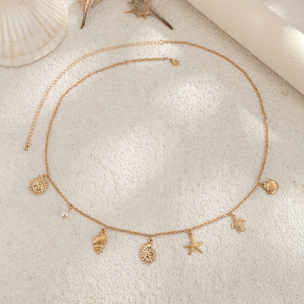 Ocean charm waist chain with gold seashell starfish turtle and pearl accents adjustable beach body chain belt for women on a beige textured surface