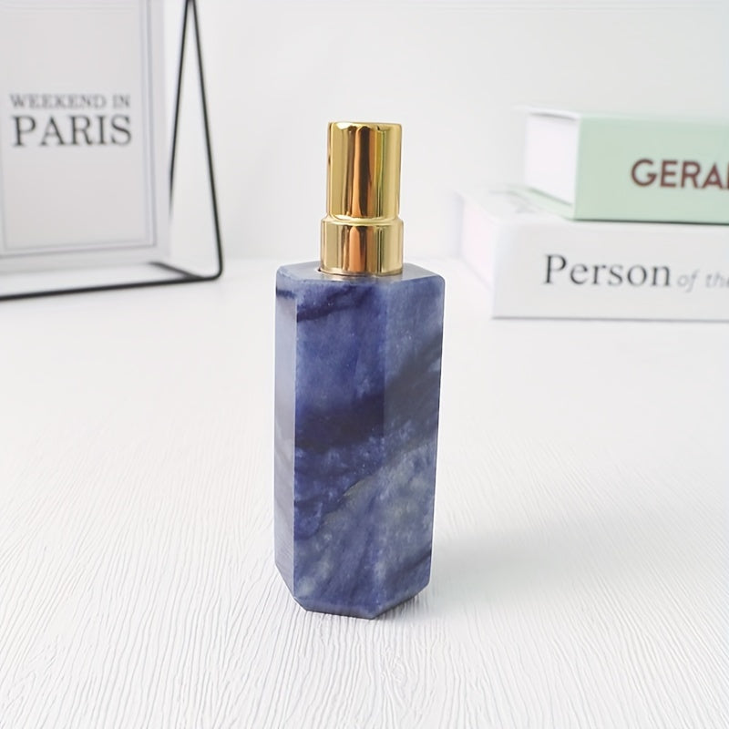A blue refillable natural crystal stone perfume bottle with stainless steel spray pump on a white background by a stack of books.