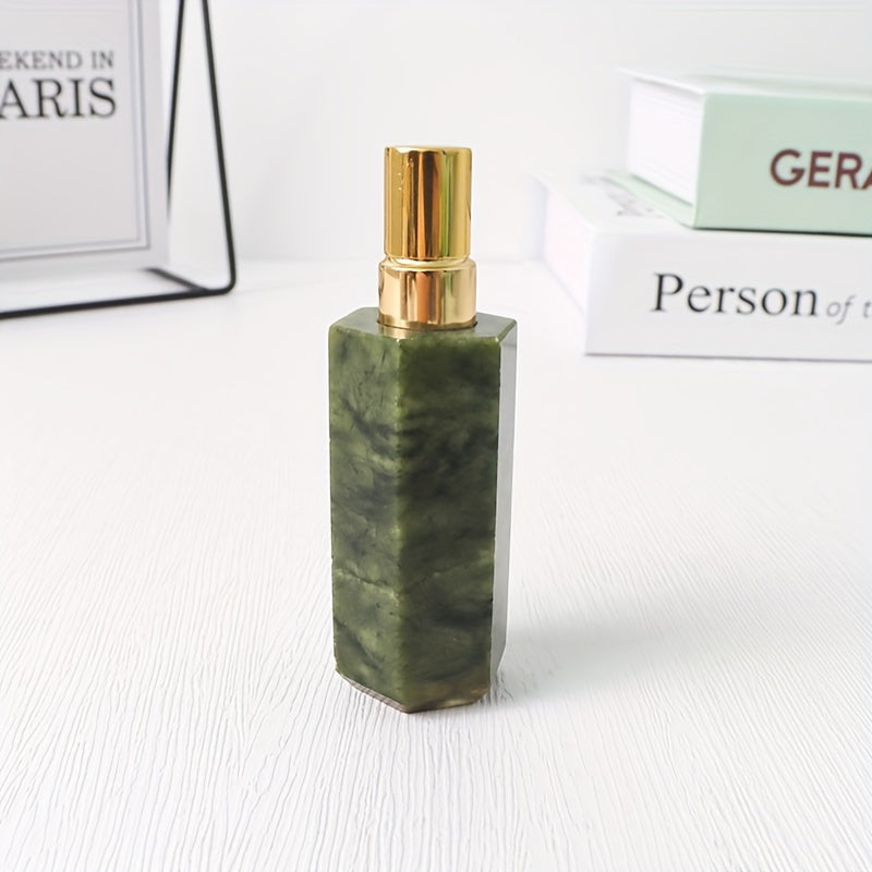 A dark green refillable natural crystal stone perfume bottle with stainless steel spray pump on a white background by a stack of books.