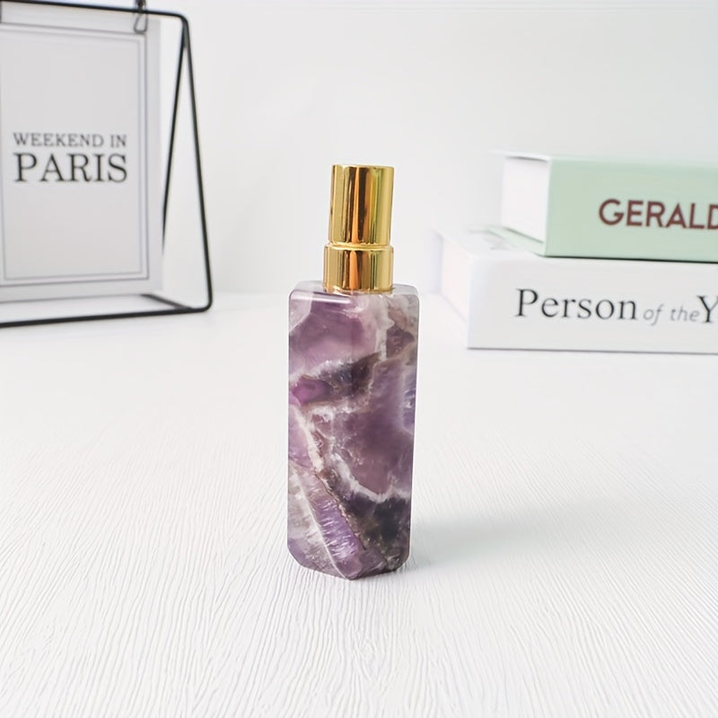 A purple refillable natural crystal stone perfume bottle with stainless steel spray pump on a white background by a stack of books.