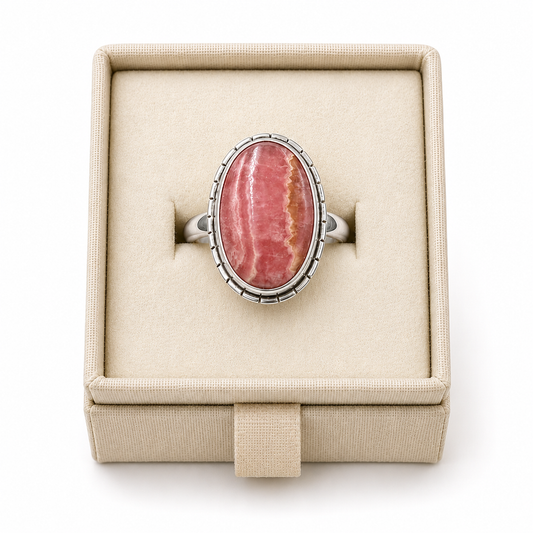Sterling silver bezel-set ring with an oval rhodochrosite cabochon displayed in a soft linen jewelry box on a white background -Clover's Charm.