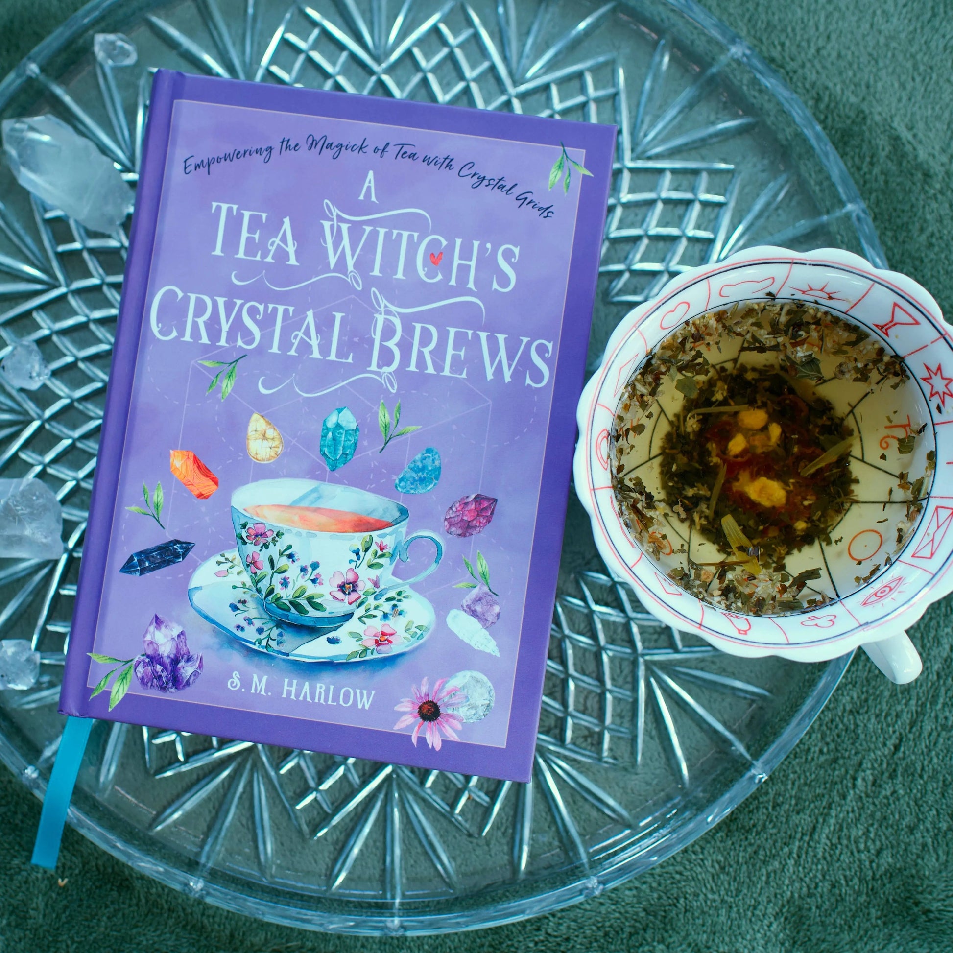 Book titled 'A Tea Witch's Crystal Brews' on a glass surface with a cup of tea.