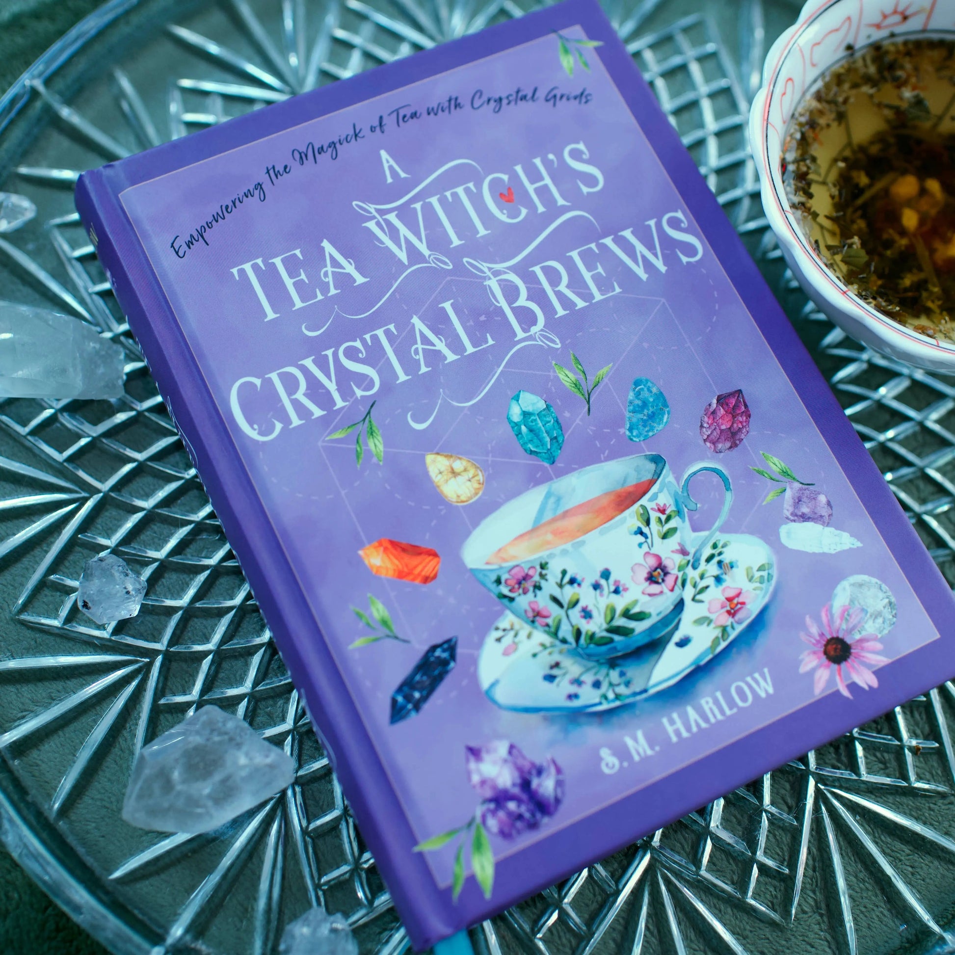 Book titled 'A Tea Witch's Crystal Brews' on a textured surface with a cup of tea.