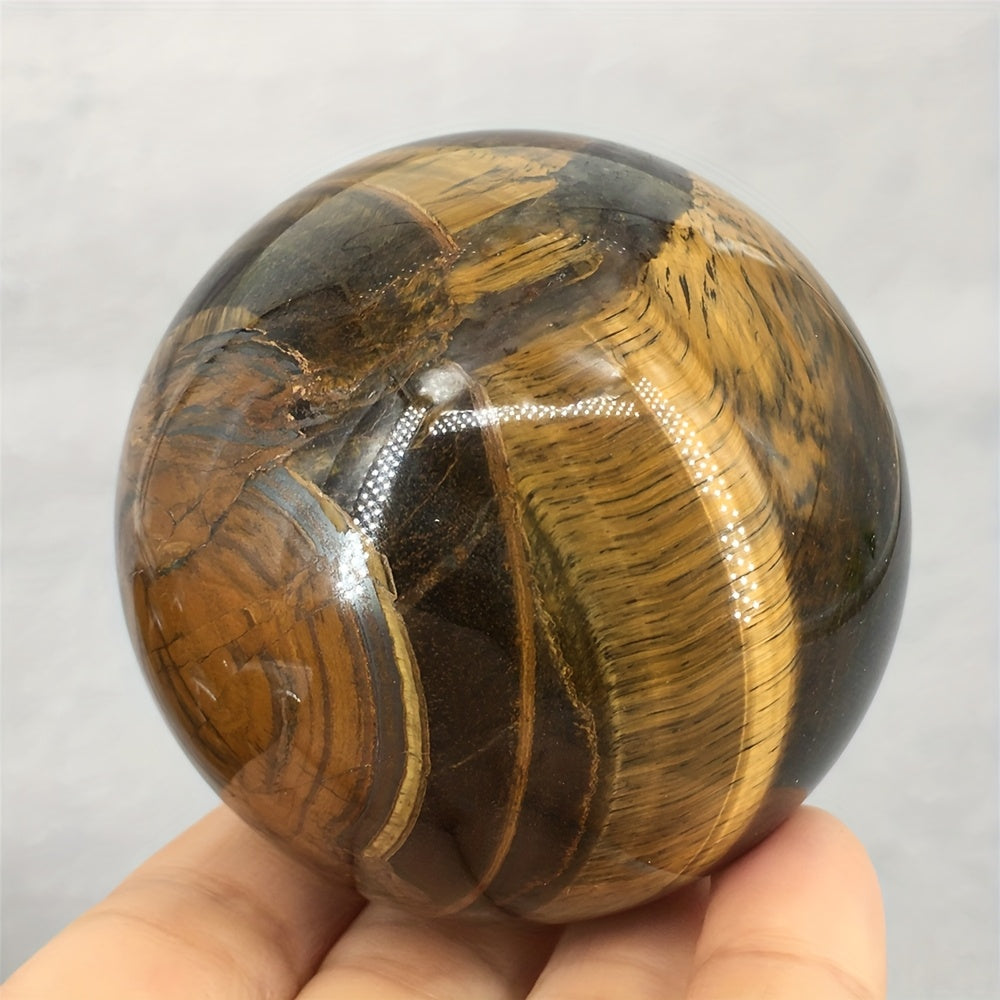Tiger's eye crystal ball resting on someone's fingertips on a white background