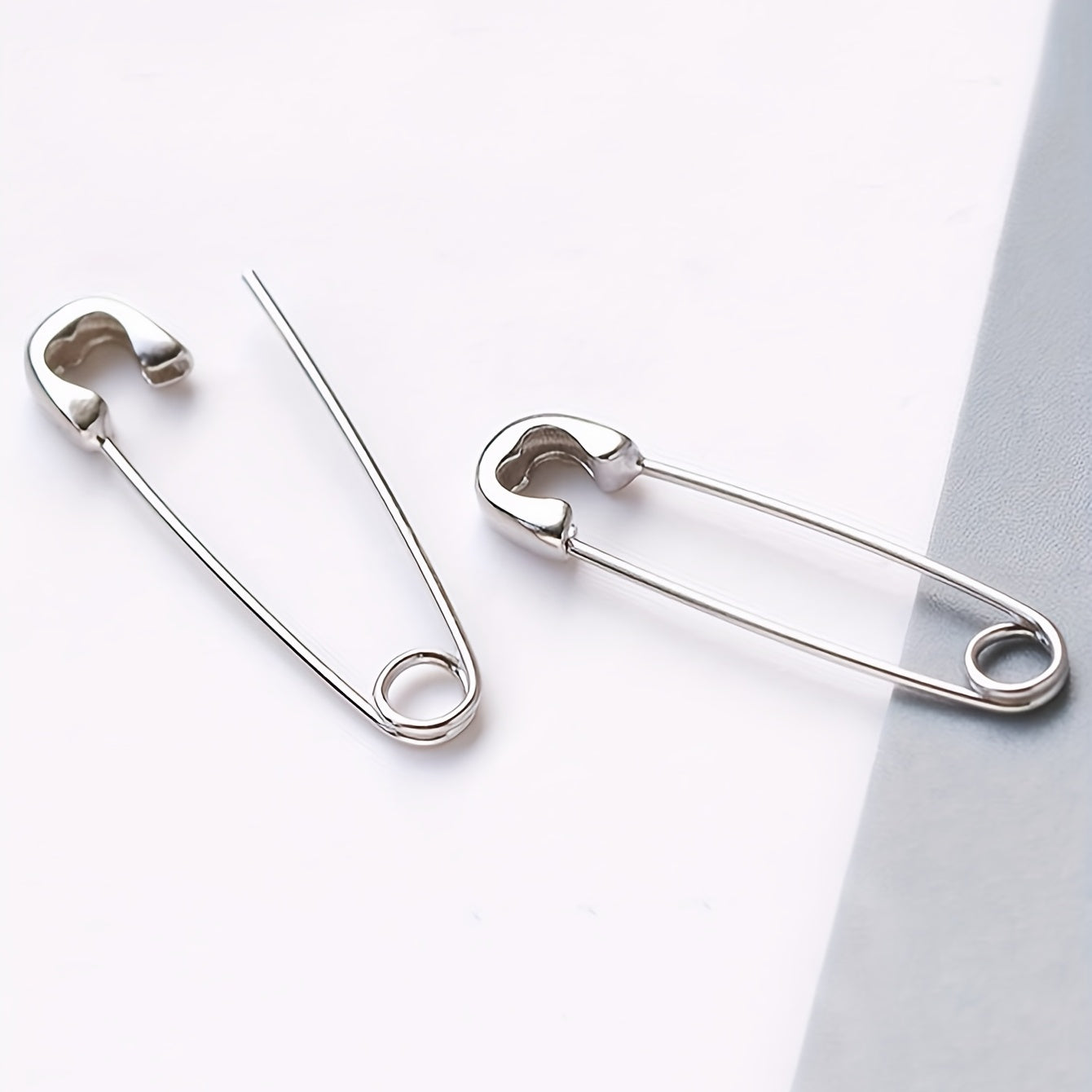 Minimalist silver-plated safety pin earrings shown at angled view on a white background