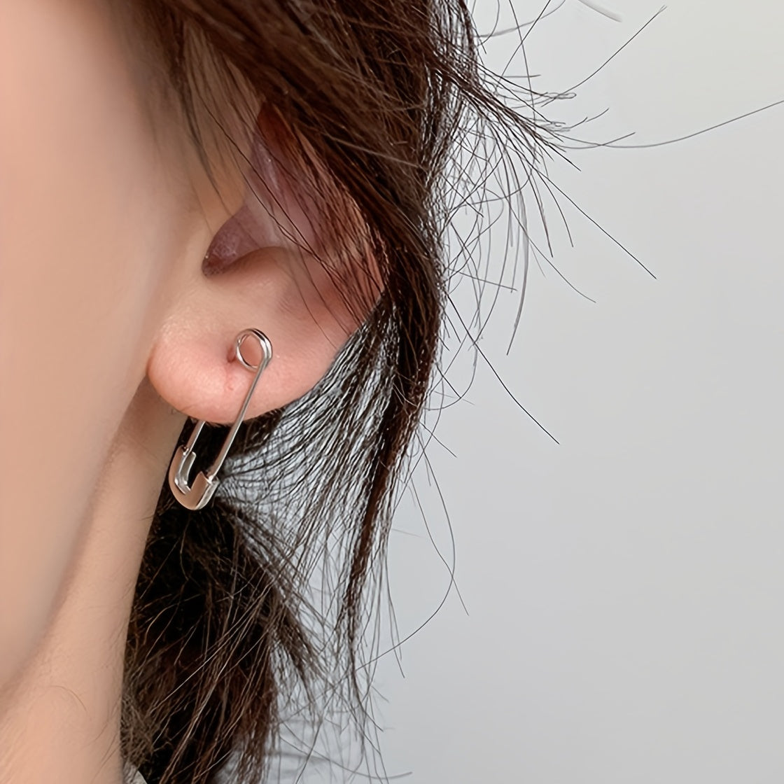 Close-up of an ear wearing a unique safety pin earring against a neutral background
