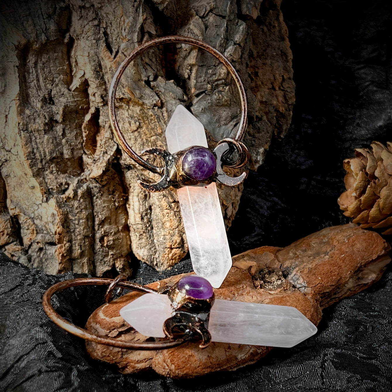 White natural crystal point moon pendant charm with faceted rock crystal and vintage style boho metal accent displayed two on a black table on bark