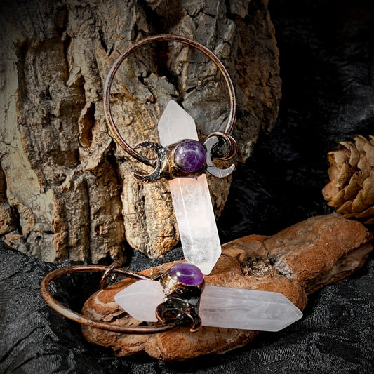 White natural crystal point moon pendant charm with faceted rock crystal and vintage style boho metal accent displayed two on a black table on bark