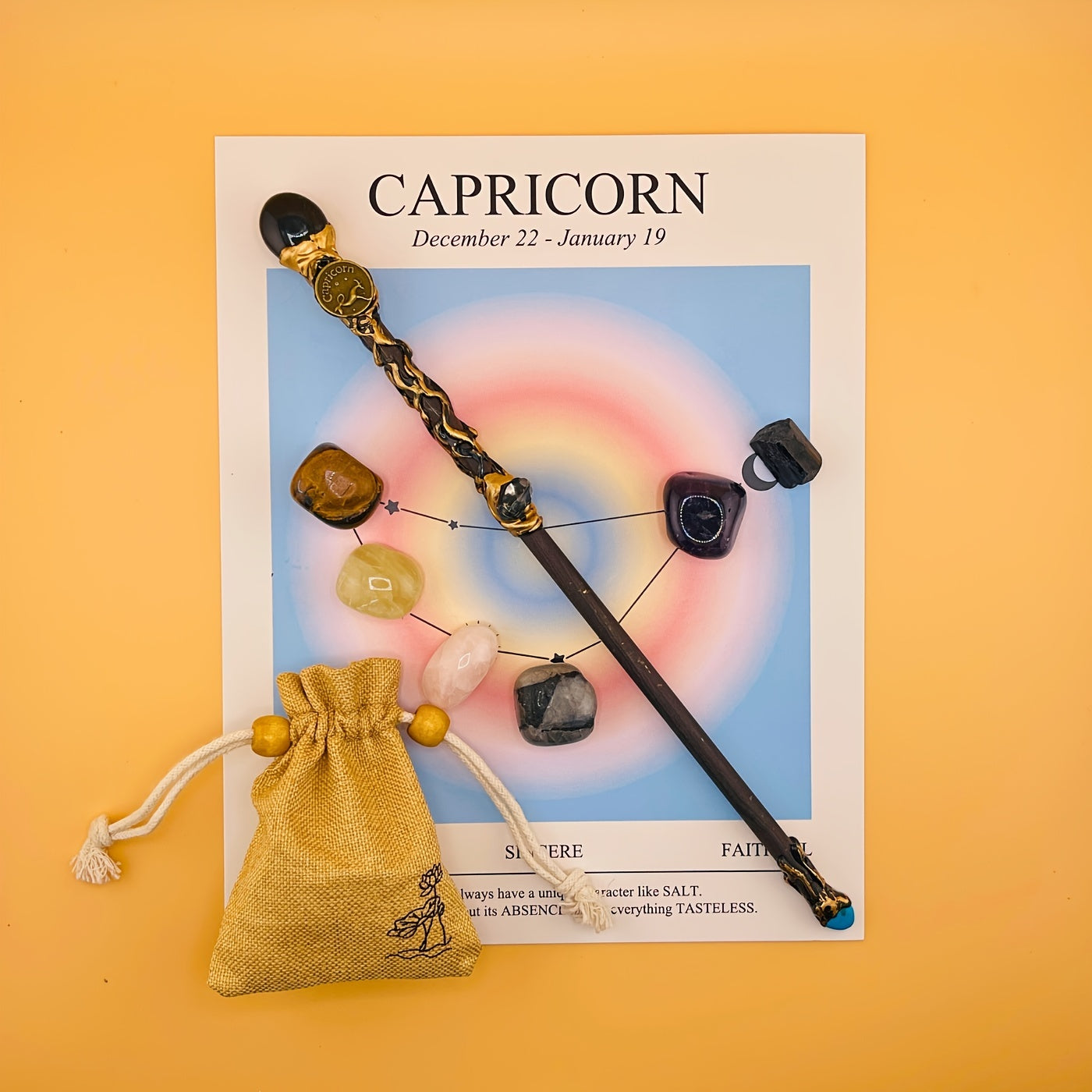 Decorative wand with stones on a Capricorn zodiac card against an orange background